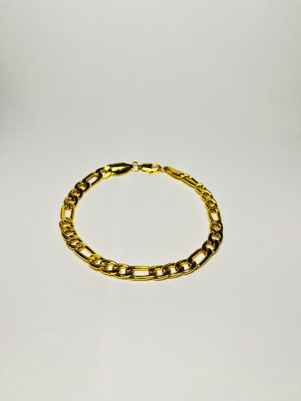 Rövid hosszú láncszemes arany karlánc letisztult, világos háttéren, minimalista kompozícióban.