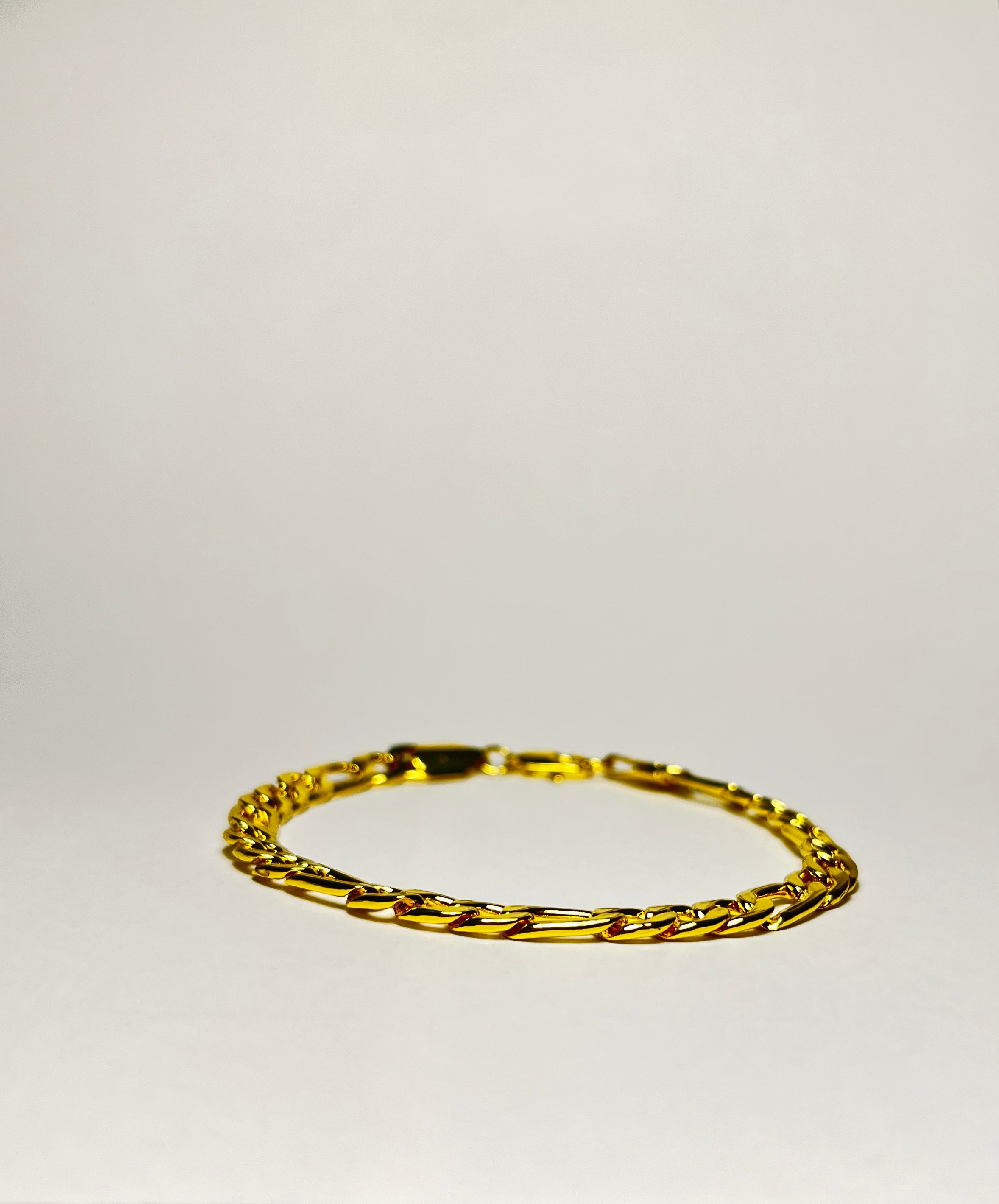 Rövid hosszú láncszemes arany karlánc letisztult, világos háttéren, minimalista kompozícióban.