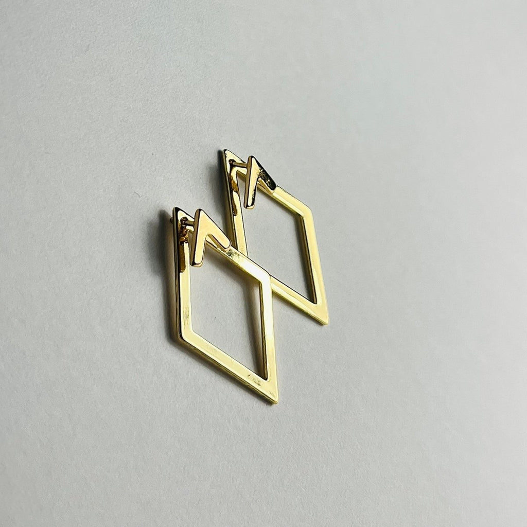 Aranyozott rombusz alakú fülbevaló pár fehér háttéren, letisztult és elegáns megjelenéssel.