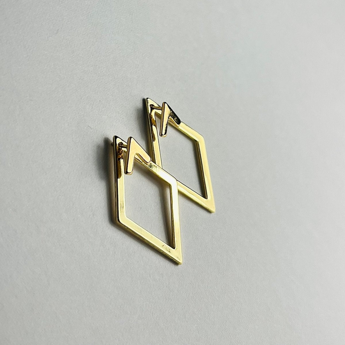 Aranyozott rombusz alakú fülbevaló pár fehér háttéren, letisztult és elegáns megjelenéssel.