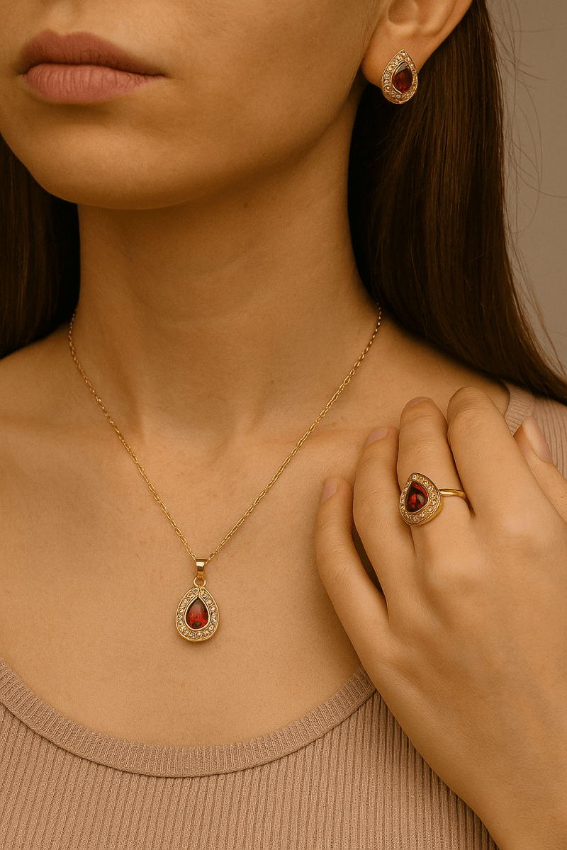 Vintage stílusú, csepp alakú piros köves nyaklánc, gyűrű és fülbevaló, egy női modell viseli, elegáns és nőies megjelenéssel, lágy természetes fényben.