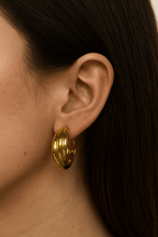 Arany csavart karika fülbevaló egy nő fülében, elegáns és kifinomult stílusban, lágy fényben fotózva.