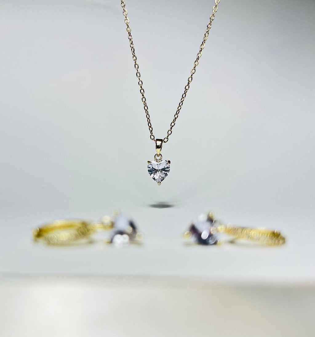 Aranyozott nemesacél szív medálos nyaklánc fehér háttéren, finom, fényes lánccal és letisztult megjelenéssel. Aranyozott szív alakú fülbevaló pár fehér háttéren, fényes felülettel, finom és nőies stílusban.