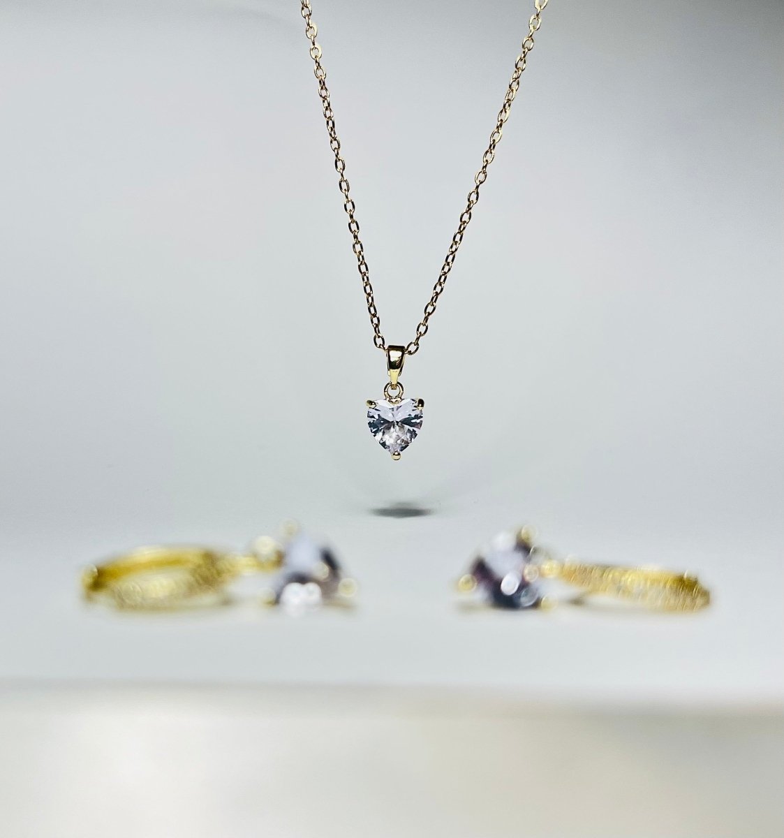 Aranyozott nemesacél szív medálos nyaklánc fehér háttéren, finom, fényes lánccal és letisztult megjelenéssel. Aranyozott szív alakú fülbevaló pár fehér háttéren, fényes felülettel, finom és nőies stílusban.